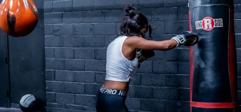 Mulher utilizando luvas de boxe e dando socos em um saco de pancada.