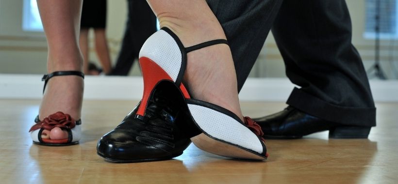 Fotografia fragmentada mostrando os pés de um casal que está dançando; a mulher usa um salto e o homem um sapato social.