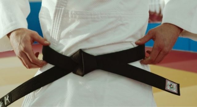 Fotografia fragmentada mostrando uma pessoa usando um kimono com a faixa na cor preta. As mãos estão segurando a faixa, que está presa à cintura.