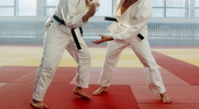 Dois lutadores competindo no tatame. Ambos vestem quimono branco com faixa preta.