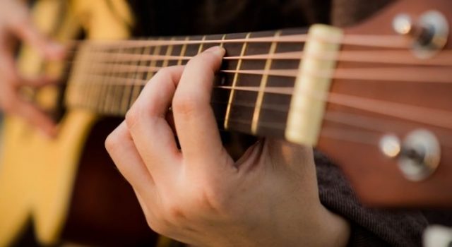 Fotografia fragmentada mostrando as mãos de uma pessoa tocando violão.