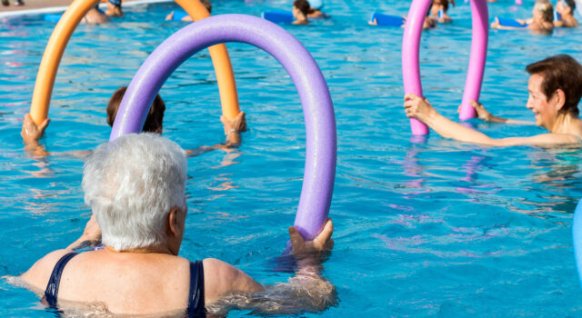 Senior Women Doing Exercise With Soft Foam Noodles In Pool.